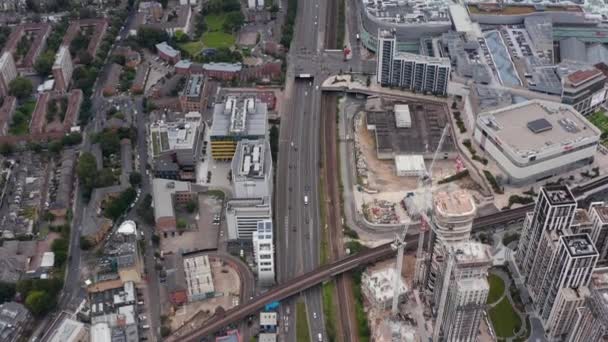 Vista aérea de la concurrida carretera de varios carriles que conduce a lo largo del sitio de construcción del proyecto de desarrollo. Inclina las imágenes hacia el puente ferroviario. Londres, Reino Unido — Vídeos de Stock