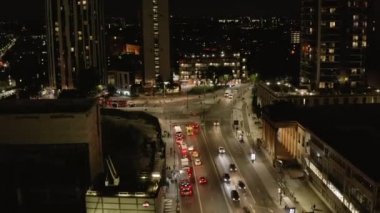 Gece şehir trafiği. Çevrede iyi aydınlatılmış yol ayrımı ve araçlar var. İleri, caddenin üzerinden uçar. Londra, İngiltere
