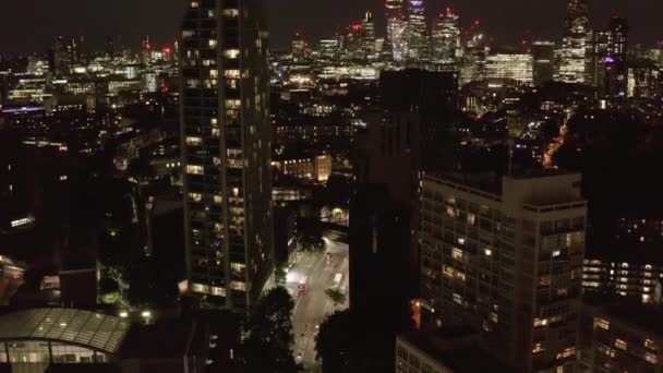 Наклон раскрытие небоскребов в центре города ночью. Вид с воздуха на улицу, ведущую между жилыми домами. Лондон, Великобритания — стоковое видео