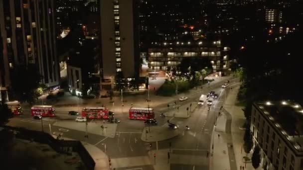 Adelante vuelan sobre la calle de la ciudad. Fila de típicos dobles pisos rojos conduciendo a través de la intercepción. Un disparo aéreo nocturno. Londres, Reino Unido — Vídeo de stock