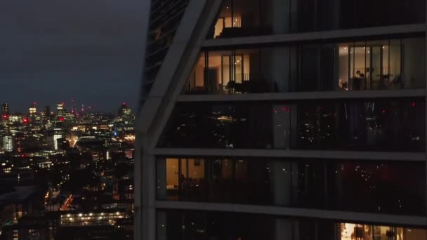 Disparo descendente a lo largo de la pared en el moderno edificio residencial de gran altura. Vista a través de ventanas en pisos de lujo. Vista nocturna de la ciudad. Londres, Reino Unido — Vídeo de stock