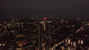 İleri sarmalar gece şehir mahallelerinin üzerinde uçar. Sahne ışıklı pencereler ve sokak lambalarıyla aydınlatıldı. Yüksek apartmana doğru gidiyor. Londra, İngiltere