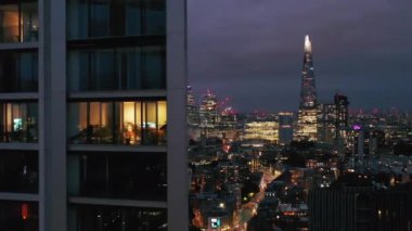 Yüksek forvetler modern yüksek apartman binasının etrafında uçar. Gece şehir manzarasının panoramik görüntüsü ortaya çıkıyor. Londra, İngiltere