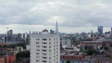 Yüksek apartmanların üzerinden uç. Şehirdeki yerleşim yerlerinin havadan görünüşü. Uzakta modern gökdelenler. Londra, İngiltere