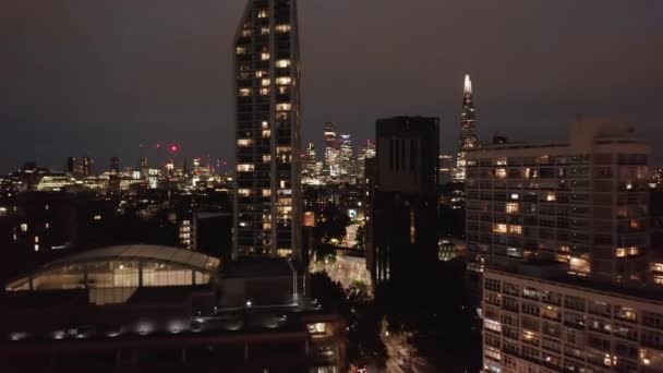 A frente voa acima da rua brilhante em torno de edifícios residenciais altos. A revelar a paisagem urbana nocturna. Londres, Reino Unido — Vídeo de Stock