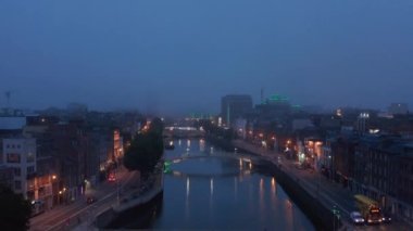 Atmosferik akşam görüntüleri. Şehirdeki Liffey Nehri 'nin aşağı inen görüntüsü ve alacakaranlıkta yaya köprüsünde yürüyen insanlar. Dublin, İrlanda