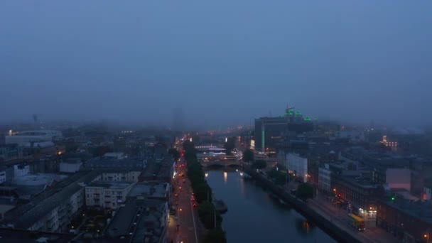 Backwards terbang di atas kota di sepanjang Sungai Liffey. Rekaman udara di malam berkabut. Tepi air berpendar. Dublin, Irlandia — Stok Video