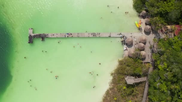 Luchtvogels oog boven hoofd naar beneden zoomend uitzicht op houten pier boven pastelgroen water. Mensen genieten van de tijd aan het water in tropische bestemming. Kaan Luum lagune, Tulum, Yucatan, Mexico — Stockvideo