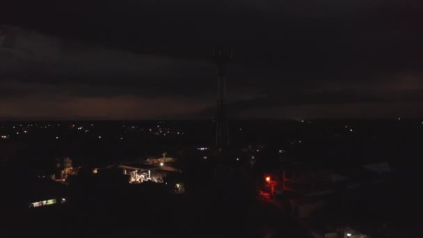 Спукла сцена телекомунікаційних щогли з антенами проти темного неба з блискавками під час шторму. Нічне місто на задньому плані. Валладолід, Мексика. — стокове відео