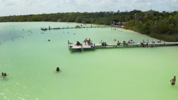 Flyg över träpirar vid sjöstranden med människor som njuter av varm solig dag. Naturlig pool med grunt vatten i tropisk destination. Kaan Luum lagunen, Tulum, Yucatan, Mexiko — Stockvideo