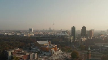 Parlak sabah güneşiyle aydınlatılan şehrin havadan panoramik manzarası. Berlin Filarmoni binalarının üzerinde ilerliyorlar. Fernsehturm TV kulesi uzakta. Berlin, Almanya