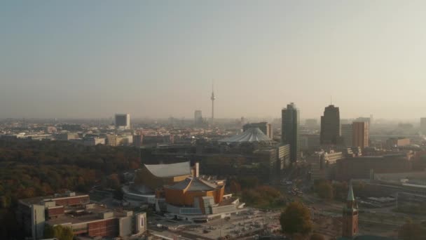 Aerial panoramic view of city lit by bright morning sun. Forwards fly above Berlin Philharmonic buildings. Fernsehturm TV tower in distance. Berlin, Germany — Stock Video