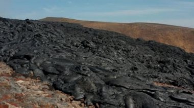 Kayalık zemindeki koyu ve sert lav akıntısının kaygan ve pan görüntülerini kaydır. Şaşırtıcı doğal fenomen, patlamış magmatik madde katmanı. Fagradalsfall volkanı. İzlanda, 2021