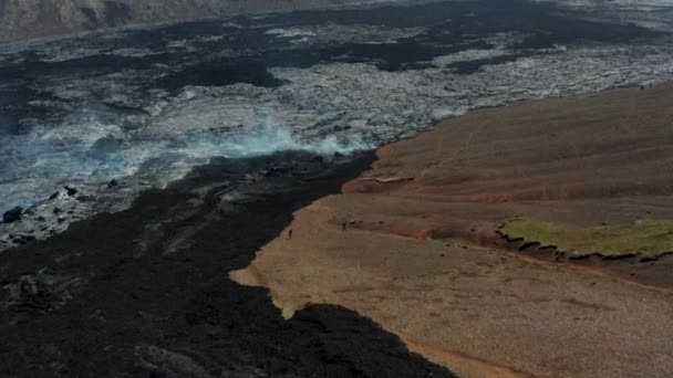 Flyg ovanför det vulkaniska landskapet. Folk som utforskar kylning av lavaströmmen. Vit rök kommer ut från naturlig ventil. Fagradalsfjallsvulkan. Island, 2021 — Stockvideo