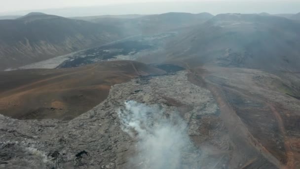 Лети над горным хребтом. Сосредоточение внимания на дыме, выходящем из отверстия в слое охлаждающей лавы в новом лавовом поле. Вулкан Фаградальсфьол. Исландия, 2021 — стоковое видео