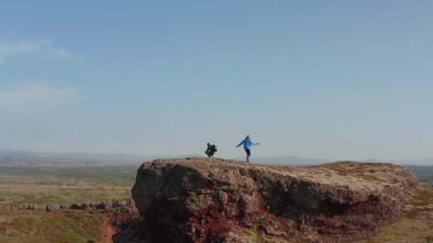 Atterraggio drone vista di due scalatori backpackers sentirsi liberi cima della collina in Islanda. Vista aerea verticale di due escursionisti che si godono la libertà su una scogliera — Video Stock