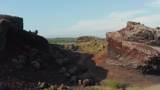 Veduta aerea drone volare verso l'uomo escursionista solo camminando sentiero in formazioni rocciose desertiche in Islanda. Uccelli occhio esploratore maschio godendo incredibile panorama e bellezza in natura in piedi sopra scogliera di pietra — Video Stock
