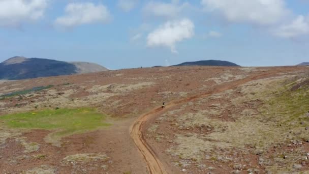 アイスランドの砂漠の緑地でモトクロスをしている人の鳥の目のビュー。山の間でオフロードバイクを運転ライダーの空中ドローンビュー — ストック動画