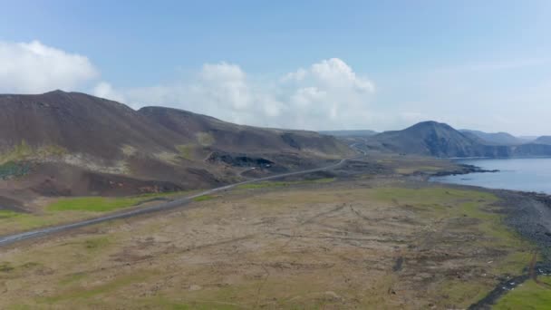 Vista aérea de la costa de iceland con playa de arena negra volcánica y carretera de circunvalación. Vuelo en dron inverso revelando algunas granjas con maquinaria agrícola — Vídeos de Stock