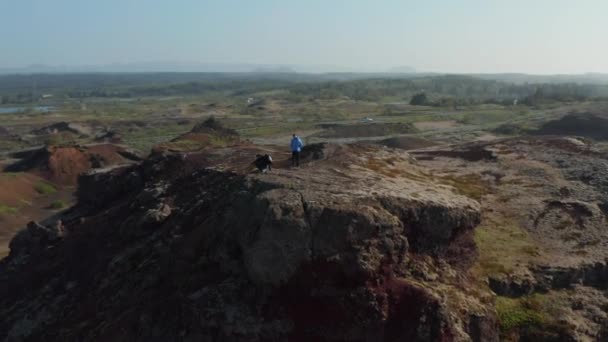 Drohnen-Vogelperspektive auf zwei junge männliche Touristen, die auf einer Klippe in Island stehen. Luftaufnahme Entdecker Wanderer Reisenden genießen ruhige und ruhig aussehende Panorama — Stockvideo