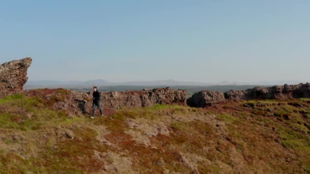 Drone view birds eye Młody człowiek Backpacker Explorer idzie ścieżką nad formacją skalną w Islandii. Widok z lotu ptaka jeden człowiek turysta wspinaczka kamienne wzgórze korzystających piękno w przyrodzie — Wideo stockowe