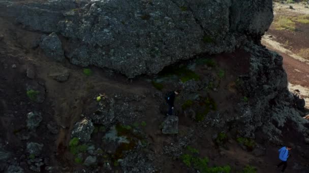 Luftaufnahme zweier Bergsteiger auf dem Weg zu einem Hügel in Island. Drohnenblick aus der Vogelperspektive: Zwei Wanderer steigen die Klippe hinunter — Stockvideo