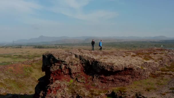 Omloppsbana drönare visa fåglar öga två män stående klippa på Island ser panorama. Flygfoto av två backpackers njuter av landskap och skönhet i naturen över kullen — Stockvideo