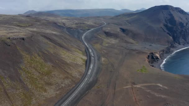 Vista aérea girando suavemente sobre Ring Road con coches conduciendo pacíficamente a través del paisaje volcánico en Islandia. Vista panorámica de la costa de Islandia con arena negra — Vídeo de stock