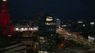 Gece şehrinin yükselen görüntüsü. Şehir merkezinde çeşitli binalar ve caddelerde trafik var. Varşova, Polonya