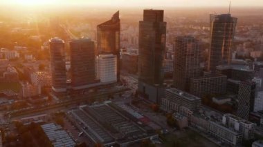Doğan güneşe karşı şehir merkezindeki bir grup gökdelen. Uzun modern ofis ya da apartman binaları. Varşova, Polonya