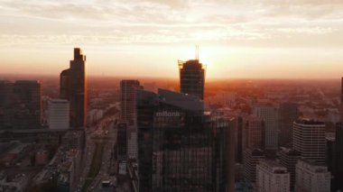 Gün batımında parlak ışığa karşı şehir merkezindeki gökdelenlerin hava görüntüleri. Geniş caddelerde trafik var. Varşova, Polonya