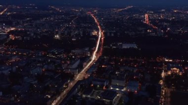 Gece şehrin görüntülerini yukarı kaldır. Kalabalık caddelerdeki trafik ışıkları sürekli kırmızı ve beyaz çizgiler oluşturuyor. Havadan panoramik çekim. Varşova, Polonya