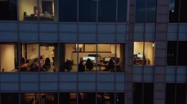 İnsanlar akşamları ofiste çalışıyor. Şehir merkezindeki yüksek, modern binanın aşağı doğru yükselişi. Varşova, Polonya