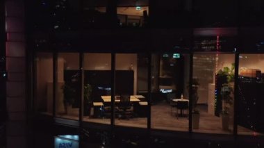 Gece şehrindeki modern yüksek katlı ofis binasının duvarları boyunca yükseliyor. Aydınlatılmış iç mekâna geniş pencerelerden bak. Varşova, Polonya