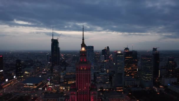 Hacia atrás vuelan por encima de la ciudad nocturna. Vista panorámica aérea de edificios del centro de gran altura al atardecer. Varsovia, Polonia — Vídeos de Stock