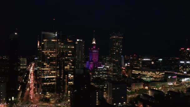 Воздушные панорамные кадры центра города с высотными зданиями ночью. Освещенный цветом исторический Дворец культуры и науки. Уорсоу, Польша — стоковое видео