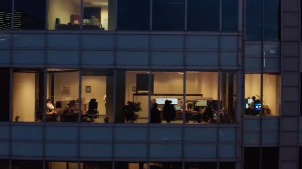 Nagranie panoramiczne okien wysokich budynków biurowych wieczorem. Ludzie w pokojach pracują po godzinach. Warszawa, Polska — Wideo stockowe