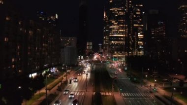 Çoklu şeritli yolun üzerinden uçarak büyük bir kasabaya doğru ilerleyin. Sokakta ve kavşakta giden arabalar. Gece şehri sahnesi. Varşova, Polonya