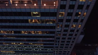 Yüksek ofis binası duvarı boyunca inen görüntüler. İnsanlar akşamları fazla mesai yapıyor. Varşova, Polonya