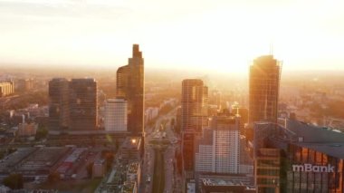 Parlak sabah güneşine karşı şehir merkezindeki yüksek binaların üzerinde ilerliyorlar. Geniş caddelerde trafik var. Varşova, Polonya