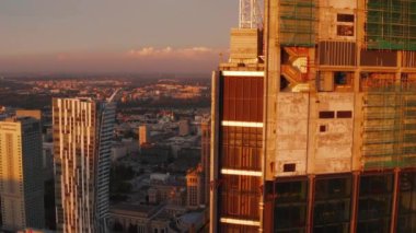 Şehrin yukarısındaki gökdelen şantiyesinin tepesine uç. Beton duvarlar ve iskele batan güneşle aydınlatılıyor. Varşova, Polonya