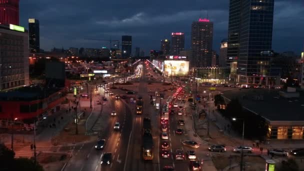 Forvetler, şehir merkezindeki yüksek ofis binaları arasında giden işlek çoklu şeritli yolun üzerinde uçuyor. Büyük kavşağın etrafındaki trafiğin akşam görüntüsü. Varşova, Polonya — Stok video