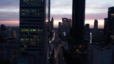 Renkli alacakaranlık gökyüzüne karşı şehir merkezindeki gökdelenler boyunca ilerliyorlar. Geniş caddede trafik yoğun. Varşova, Polonya