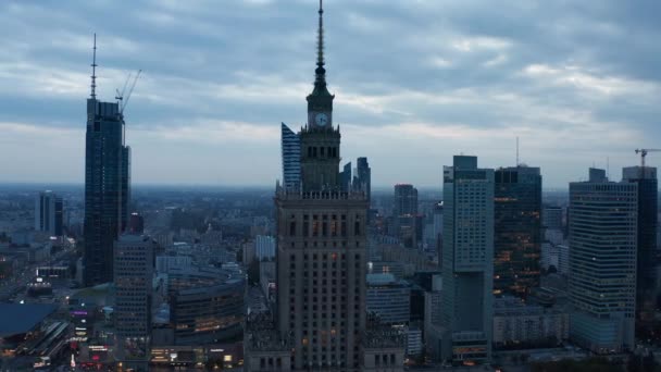 夕暮れ時の文化科学宮殿の高床式のスライドとパンショット。尖塔とタワークロックと古い高層ビル。近代的な高層ビルを背景に。ポーランドのワルシャワ — ストック動画