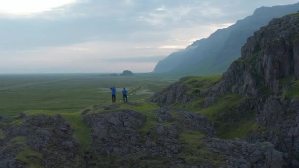 Drone view omloppsbana runt två män turist stående topp ta bild ser fantastisk dimmig panorama på Island. Flygfoto kreativa människor klättrare stående kulle ta bilder att göra minnen — Stockvideo