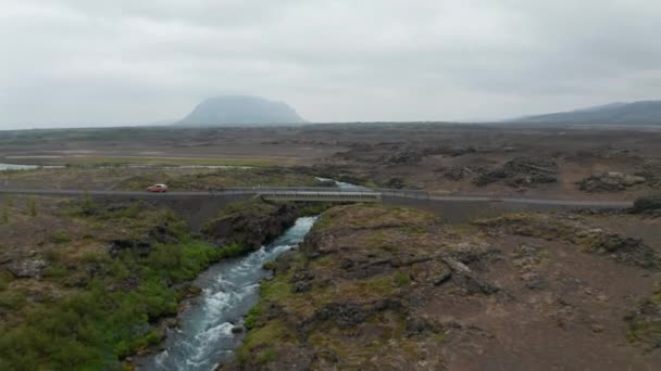 Drone uitzicht rivier stroomt over rotsachtige en verlaten landschap in IJsland. Luchtfoto IJslands landschap met rotsformaties en rivier stroomt onder ringweg brug — Stockvideo
