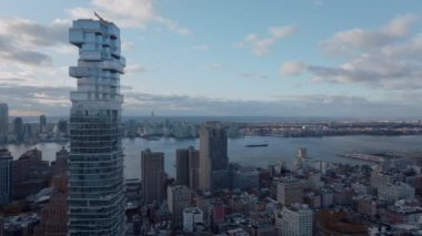 Camdan yansıtıcı cepheli modern yüksek katlı Jenga binasının kayması. Şehirleri bölen geniş bir nehir. Manhattan, New York City, ABD