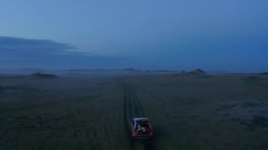 İzlanda 'nın çimenli, sisli kırsalına park edilmiş hava manzaralı bir araba. İzlanda 'daki ay manzarası vadisinin dramatik sisli, sisli dronu.