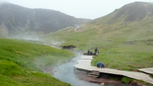Vista drone de Reykjadalur rio térmico quente que flui através do vale na Islândia. Vista aérea do rio quente geotérmico natural em Reykjadalur Valley com passadiço de madeira e vestiários — Vídeo de Stock
