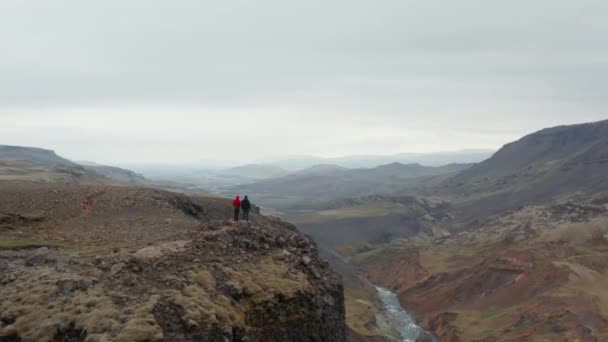 Luchtfoto vliegen in de richting van twee toeristische wandelaar genieten van een prachtig panorama van Fossa rivier vallei in IJsland. Drone uitzicht onthullend prachtig panorama van de rivier stroomt in ijzige mossige landschap — Stockvideo